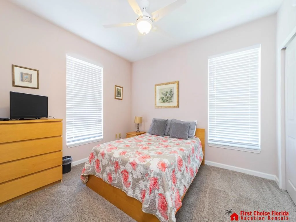 Bedroom features a floral quilted bed, light wood furniture, gray carpet, and ceiling fan with light.