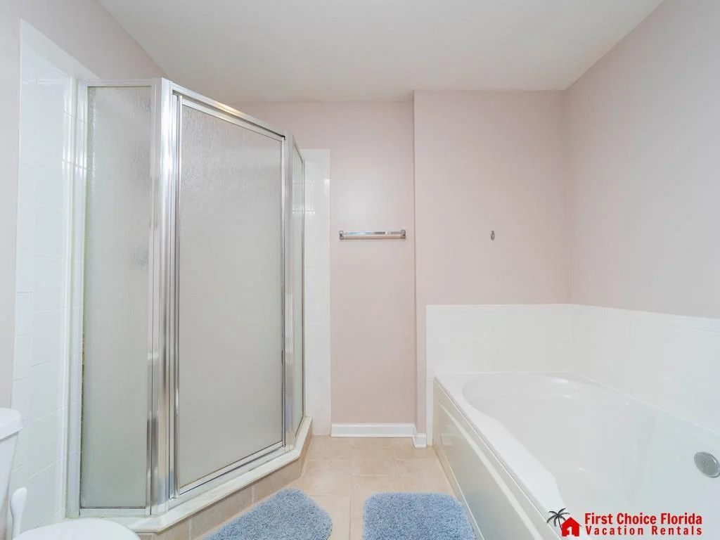 Bathroom features a corner shower with frosted glass doors and a white tiled bathtub surround.