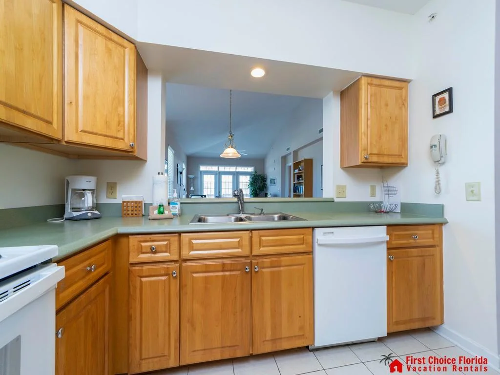 Maple cabinets frame a double stainless steel sink set in sage green laminate countertops with a dishwasher beneath.
