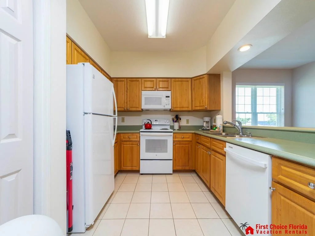 U-shaped kitchen with honey wood cabinets, white appliances, green laminate counters, and tiled floor.