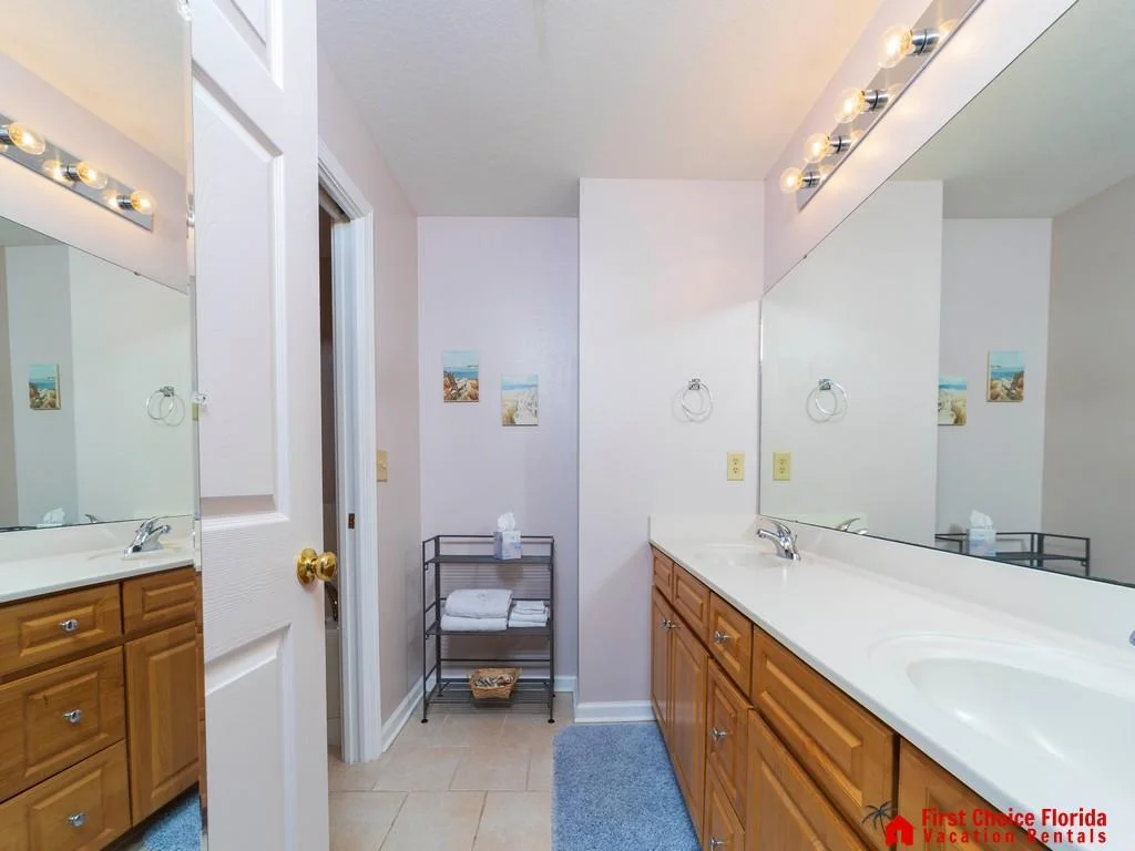 Long white countertop with dual sinks and honey wood cabinets beneath a large wall mirror.