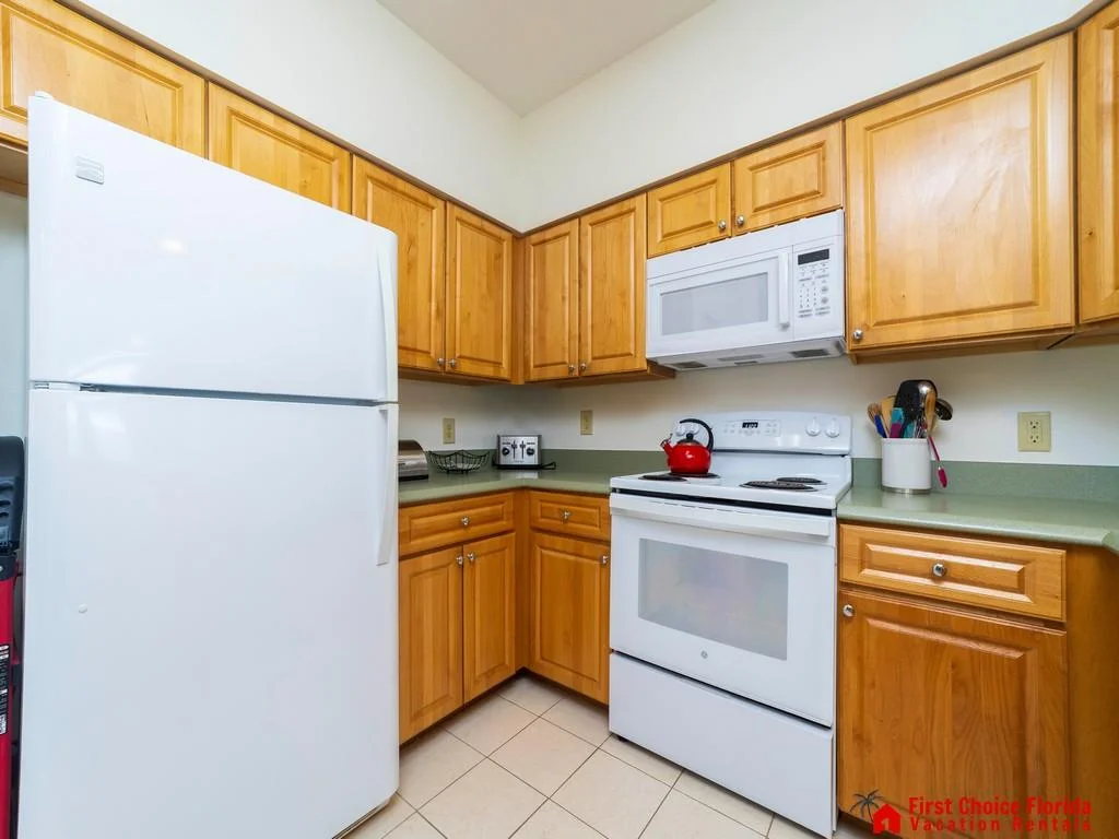 Light wood cabinets and sage green countertops surround white appliances including a refrigerator, stove, and microwave.