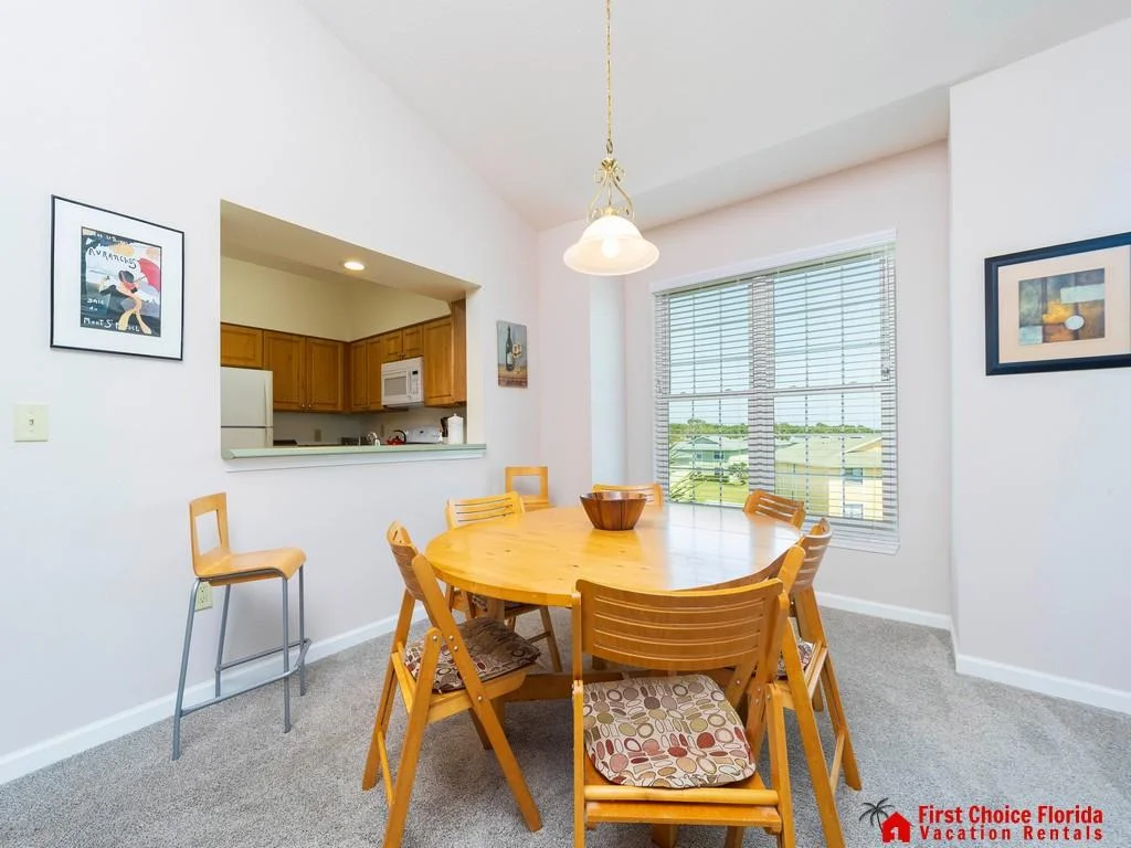 Round wooden dining table with six chairs and patterned seat cushions under a hanging light fixture.