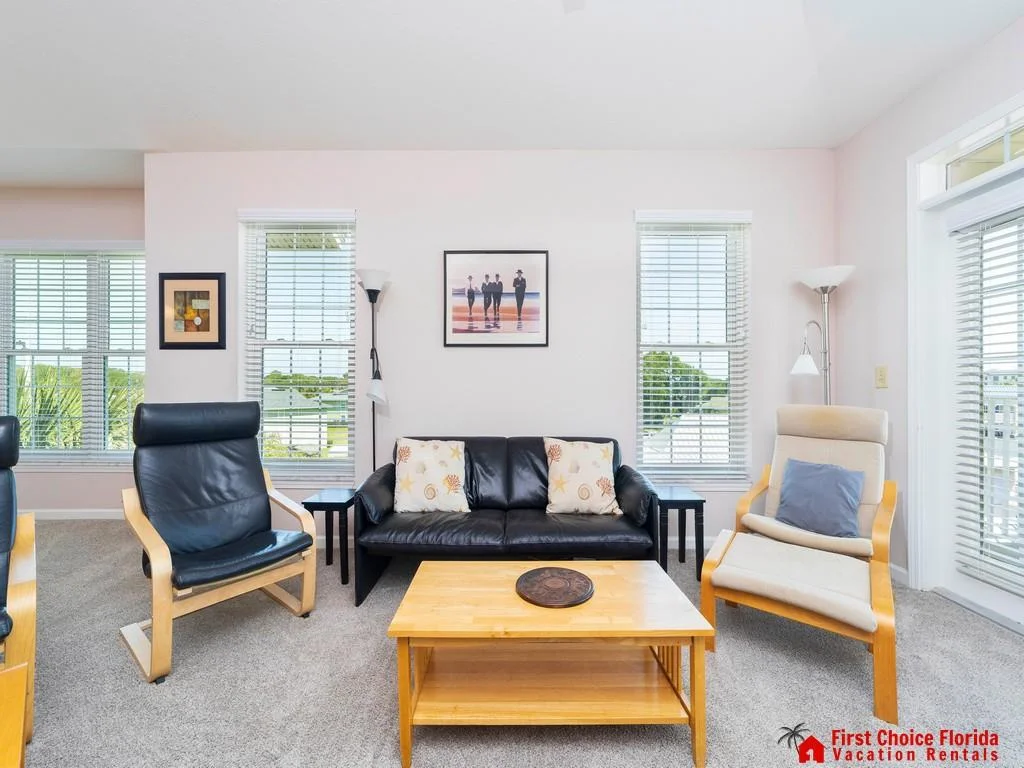 Black leather sofa and light wood-framed chairs face a honey-toned coffee table beneath coastal-themed artwork.