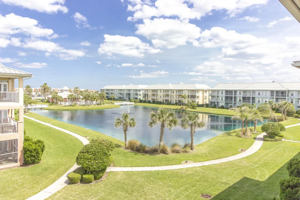 View from the balcony overlooks a pond with a central fountain, palm trees, and walking paths through green lawns.