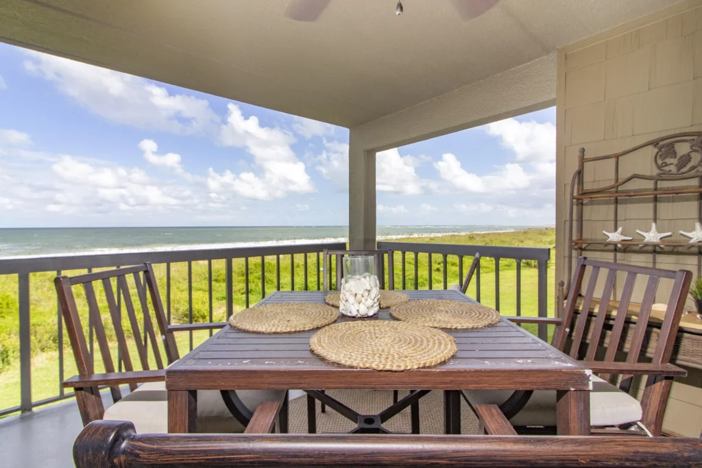 Dark wood shelving unit with decorative starfish stands beside balcony dining set and ocean views.