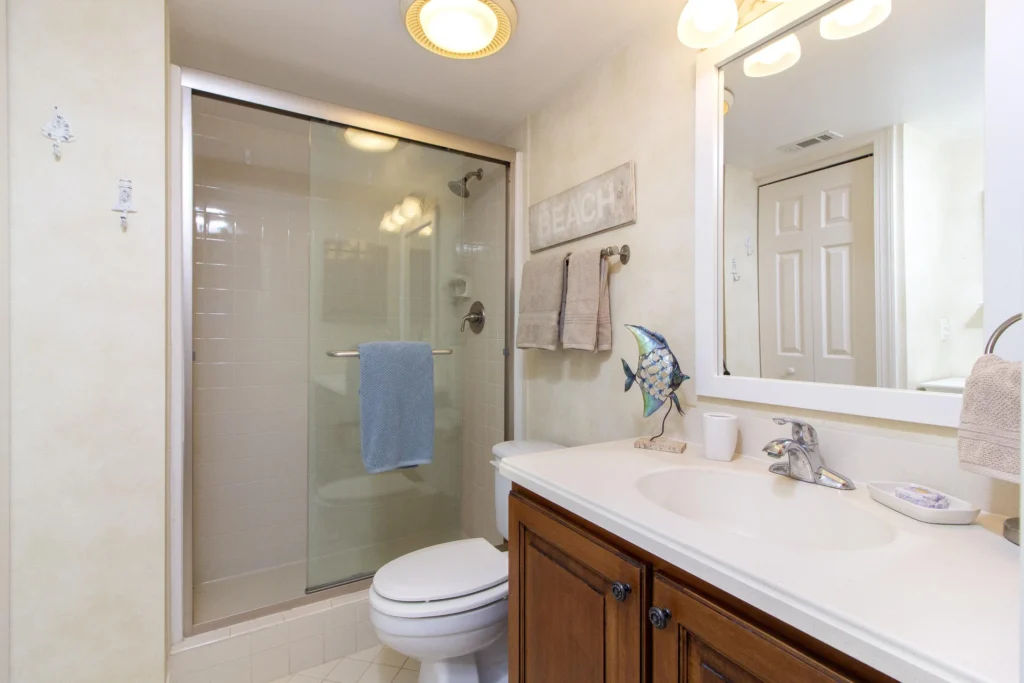 Bathroom featuring a glass sliding shower door, white tile surround, wood vanity with white countertop, and decorative fish sculpture.