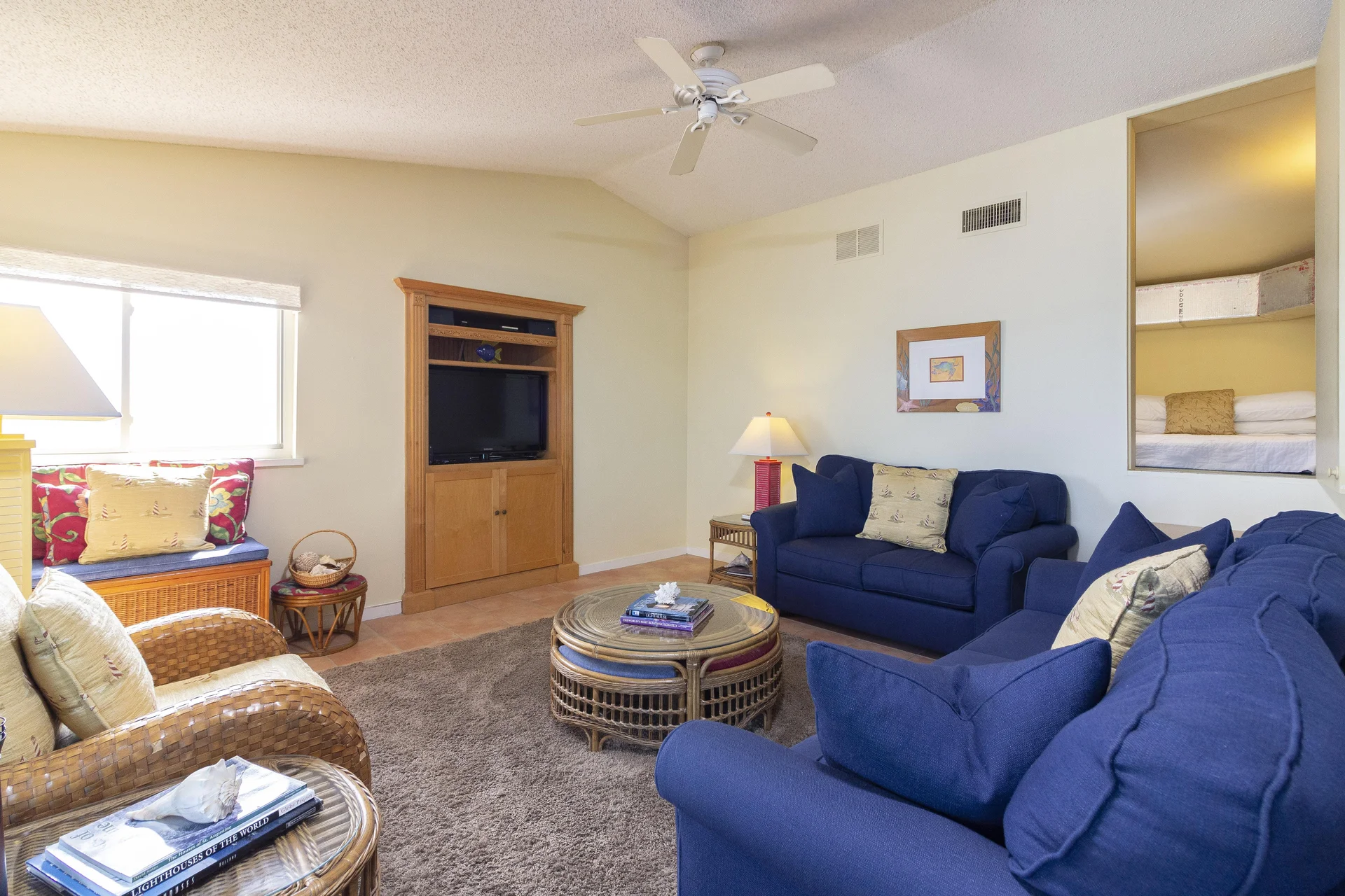 Rattan armchairs and a matching round coffee table rest on a textured brown rug beneath a white ceiling fan.