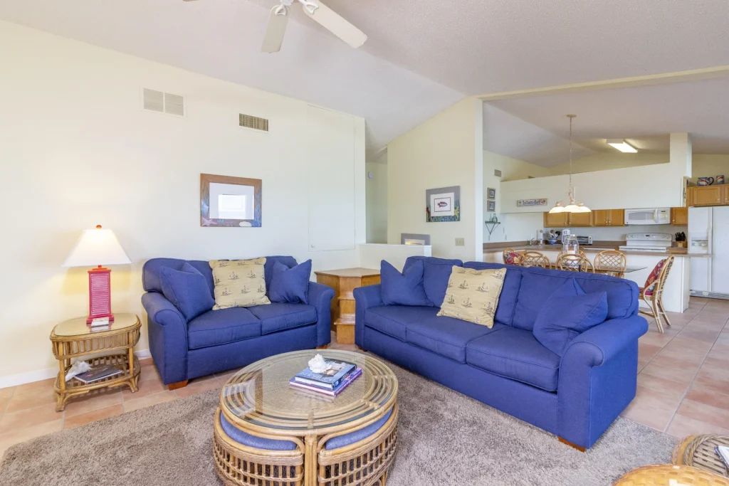 Two blue upholstered sofas face a round wicker coffee table on a plush taupe rug in the living area.