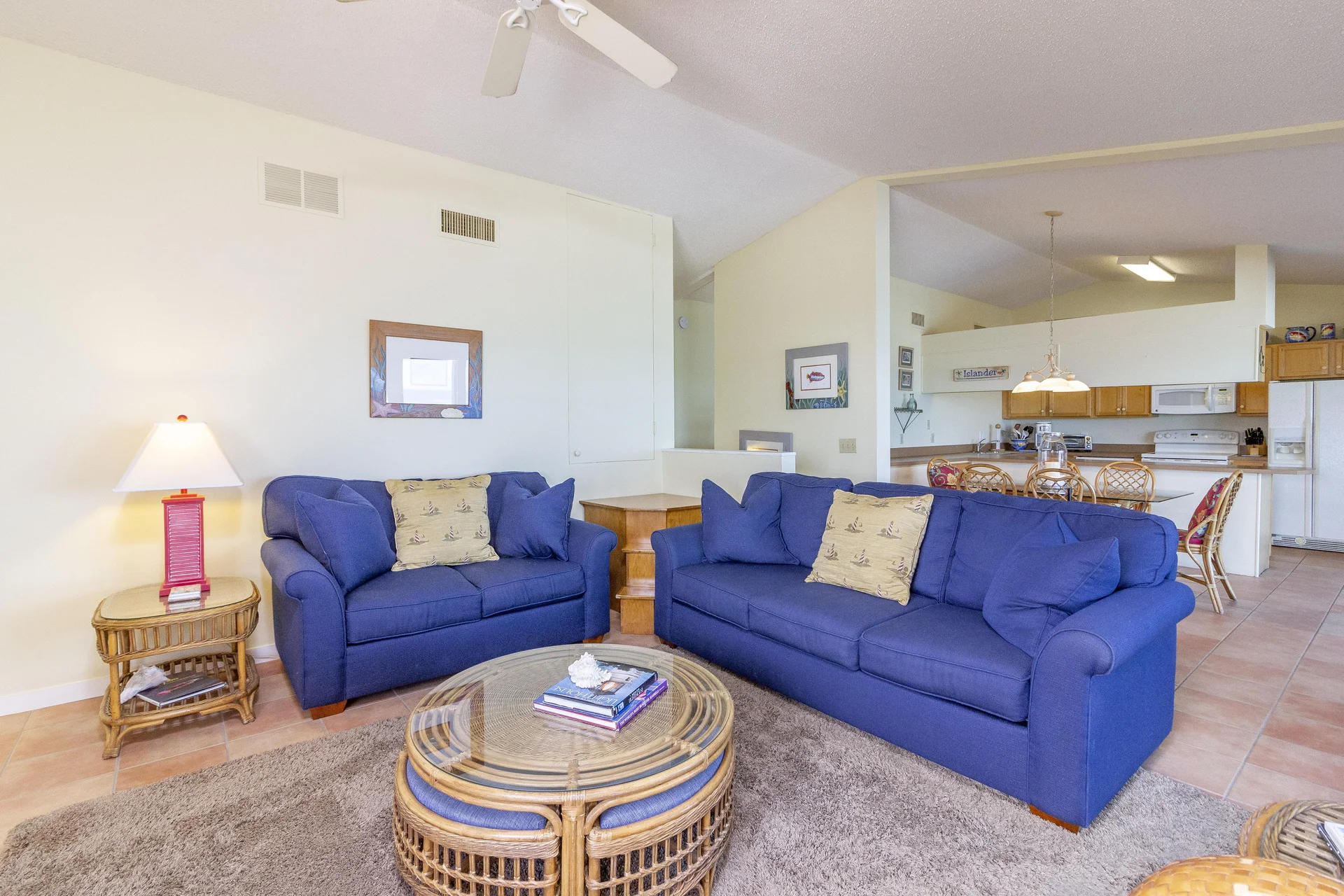 Two blue upholstered sofas face a round wicker coffee table on a plush taupe rug in the living area.