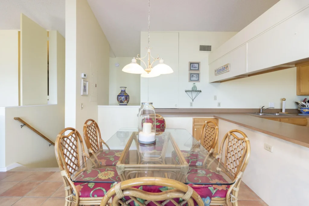 Tile flooring extends beneath a glass-top rattan dining table with floral cushions, illuminated by a three-light chandelier.
