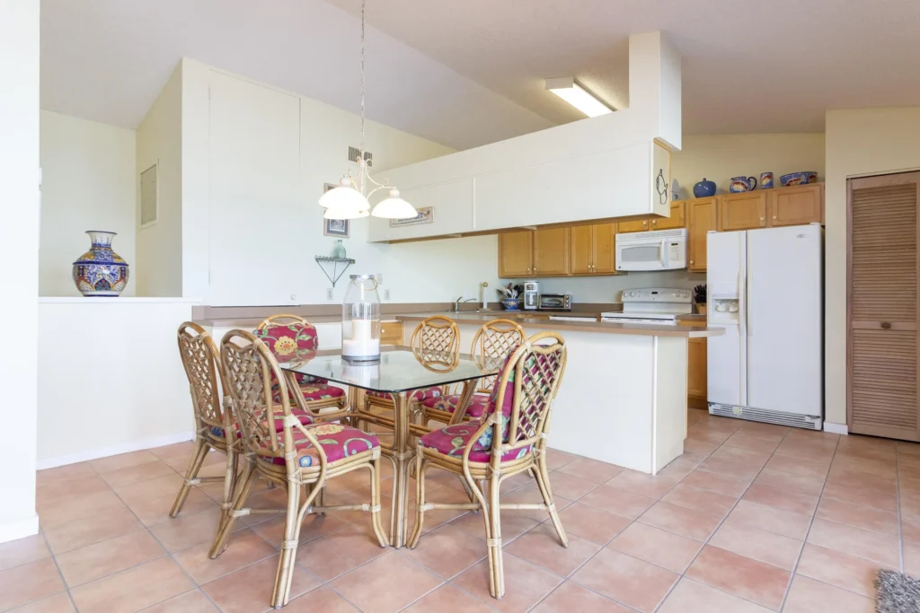 Glass-top dining table surrounded by six rattan chairs with red floral cushions on terracotta tile floor.