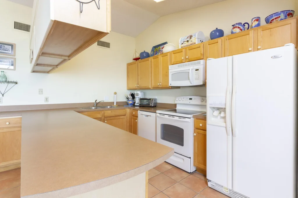 Kitchen with light wood cabinets, white appliances, tan laminate counters, and ceramic tile flooring.