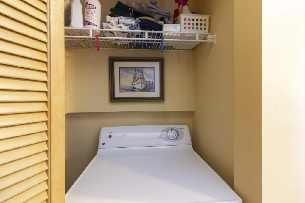 Laundry closet with white top-loading washer, beige walls, and a framed nautical print above the appliance.