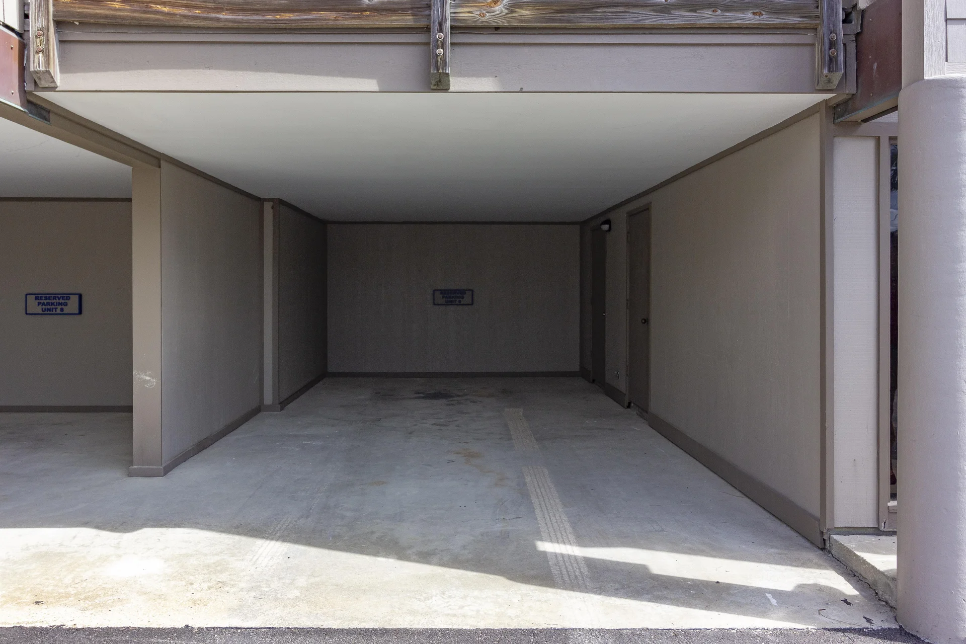 Covered parking space with smooth concrete floor, taupe walls, and adjacent storage doors.