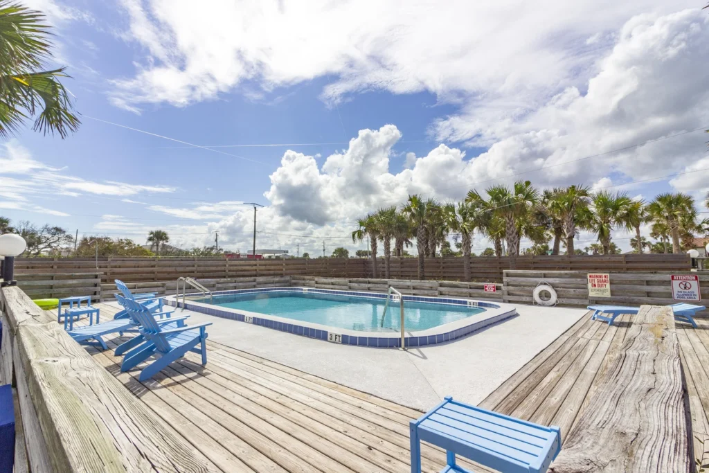 Communal pool with blue tile trim surrounded by weathered wood decking and bright blue Adirondack chairs.