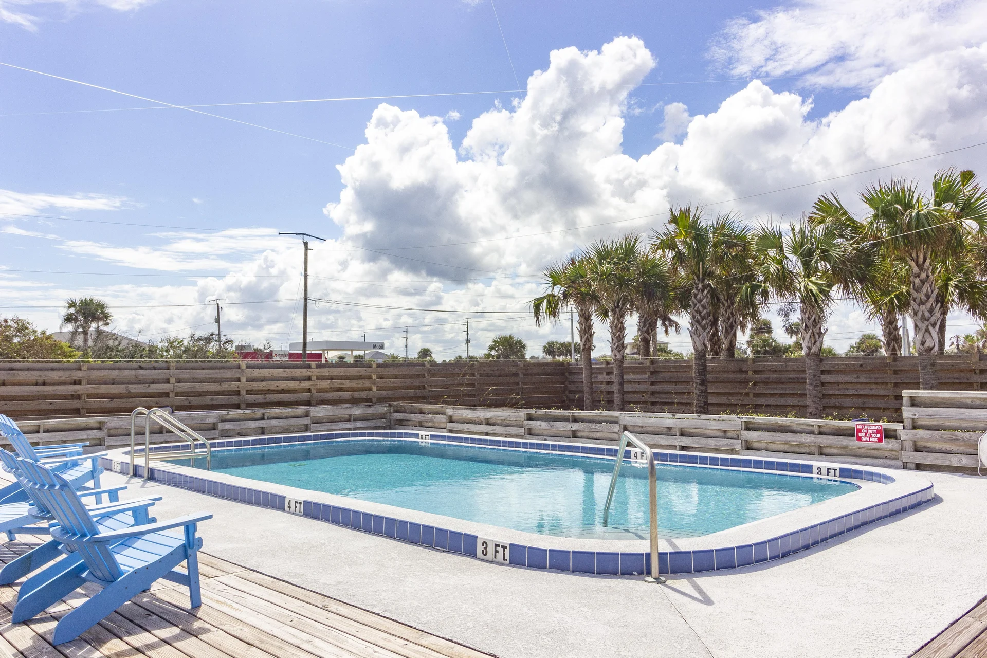 Rectangular pool with light blue tile trim, surrounded by wooden deck and blue Adirondack chairs.