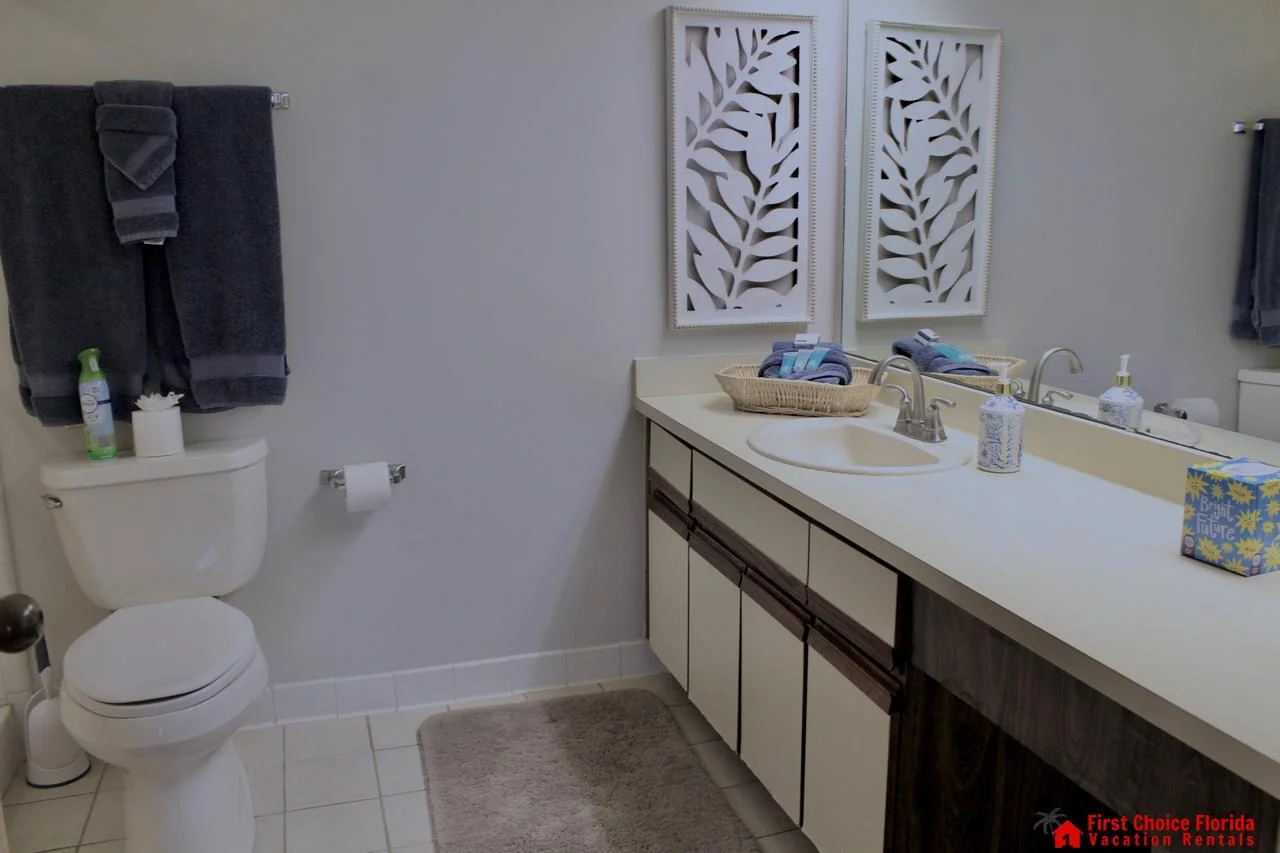 Bathroom featuring a white tile floor, long cream vanity with sink, and decorative leaf wall art above the counter.
