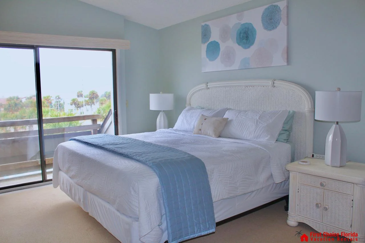 Soft blue walls complement the woven rattan headboard and matching nightstands beside sliding glass doors to the balcony.