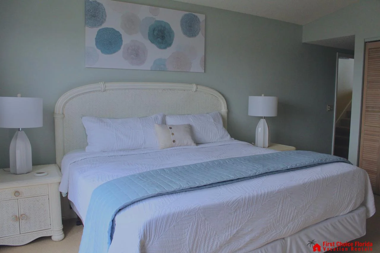 King bed with white textured bedding and pale blue throw, flanked by matching lamps on woven nightstands.