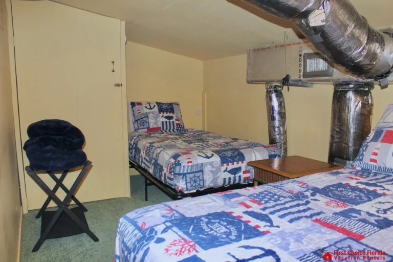 Small bedroom with twin beds dressed in nautical-themed quilts beneath exposed silver HVAC ducts.
