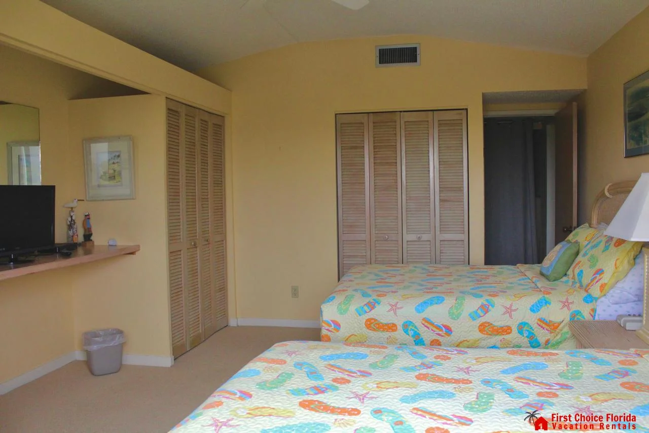 Wall-mounted TV sits atop a wooden ledge across from twin beds with colorful flip-flop patterned bedding.