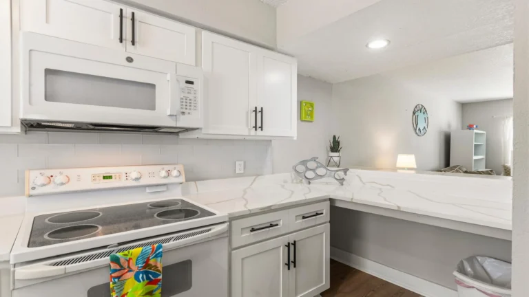 White cabinetry with black hardware surrounds a smooth electric stovetop and built-in microwave in the kitchen.