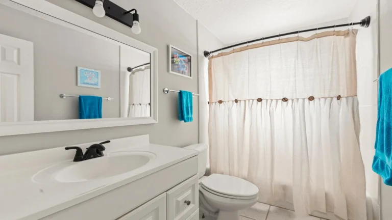 Full bathroom with white vanity, black faucet, beige fabric shower curtain, and turquoise towels.