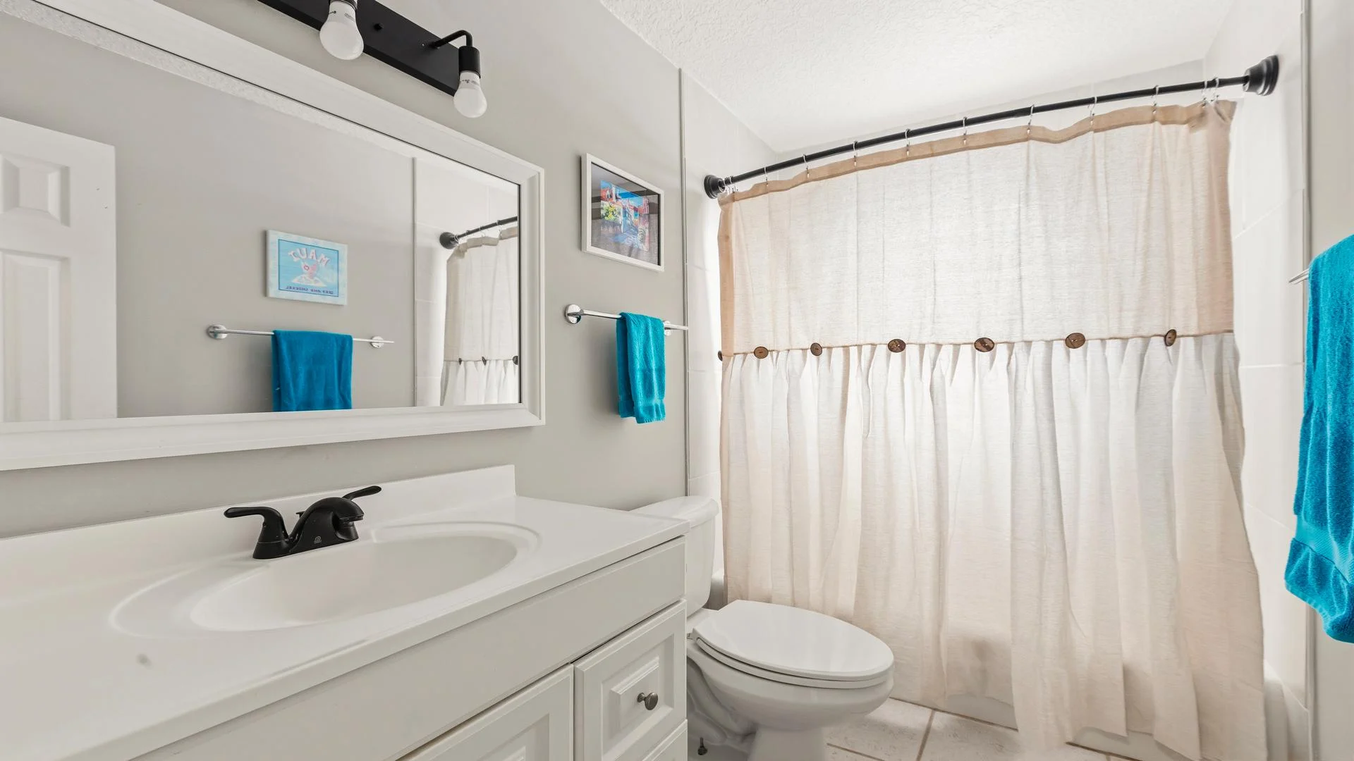 Full bathroom with white vanity, black faucet, beige fabric shower curtain, and turquoise towels.