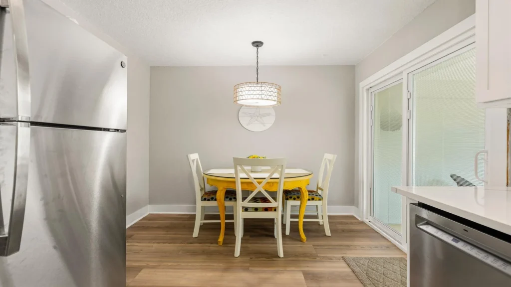 Yellow wooden dining table with white chairs featuring polka dot cushions under a woven pendant light.