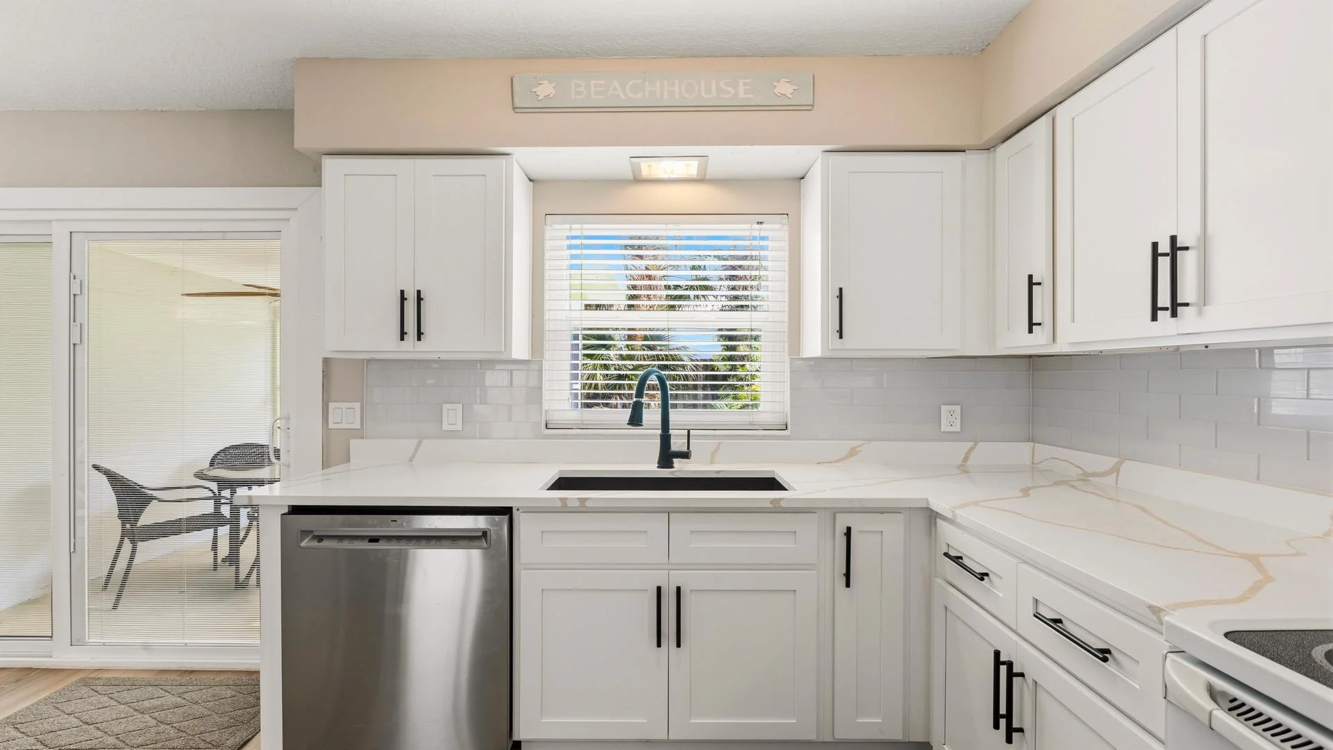 Kitchen features marble-look countertops, white subway tile backsplash, black faucet, and sliding door to patio.