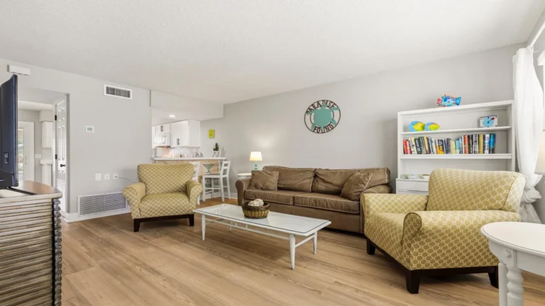 Living room with wood-look flooring, patterned yellow armchairs, brown sofa, and white coffee table.
