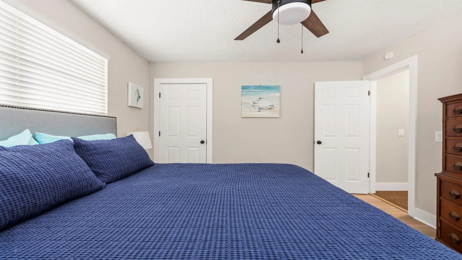King bed with textured navy bedding faces white closet doors and a wooden chest of drawers under a ceiling fan.