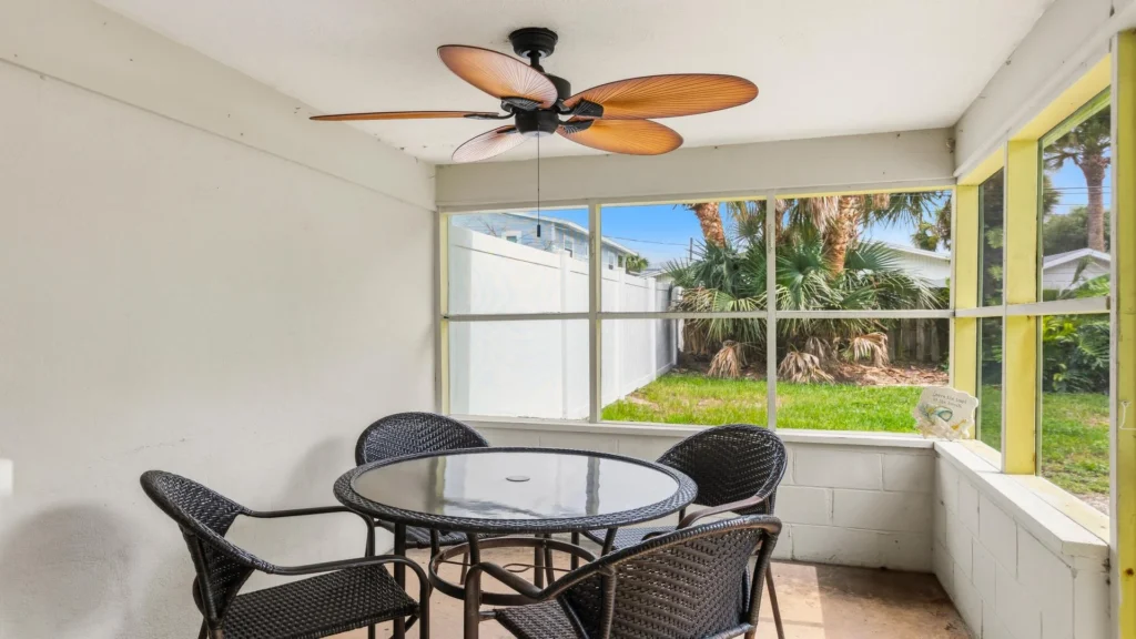 Screened porch with black wicker dining set, concrete floor, and a ceiling fan overlooking a fenced yard.