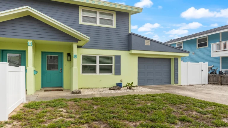 Exterior view of the townhome with blue and green siding, teal front door, single-car garage, and a small front yard.