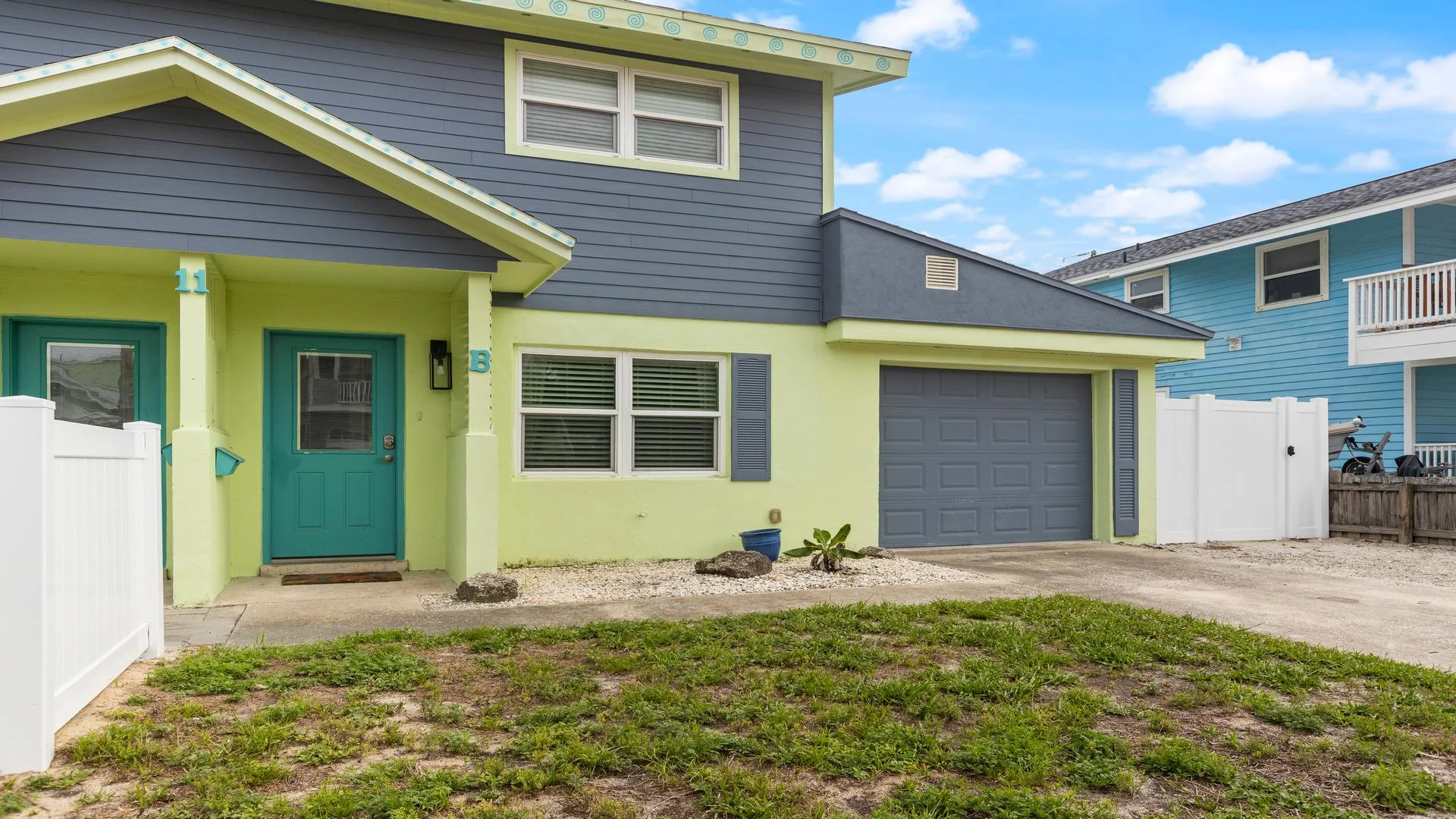 Exterior view of the townhome with blue and green siding, teal front door, single-car garage, and a small front yard.