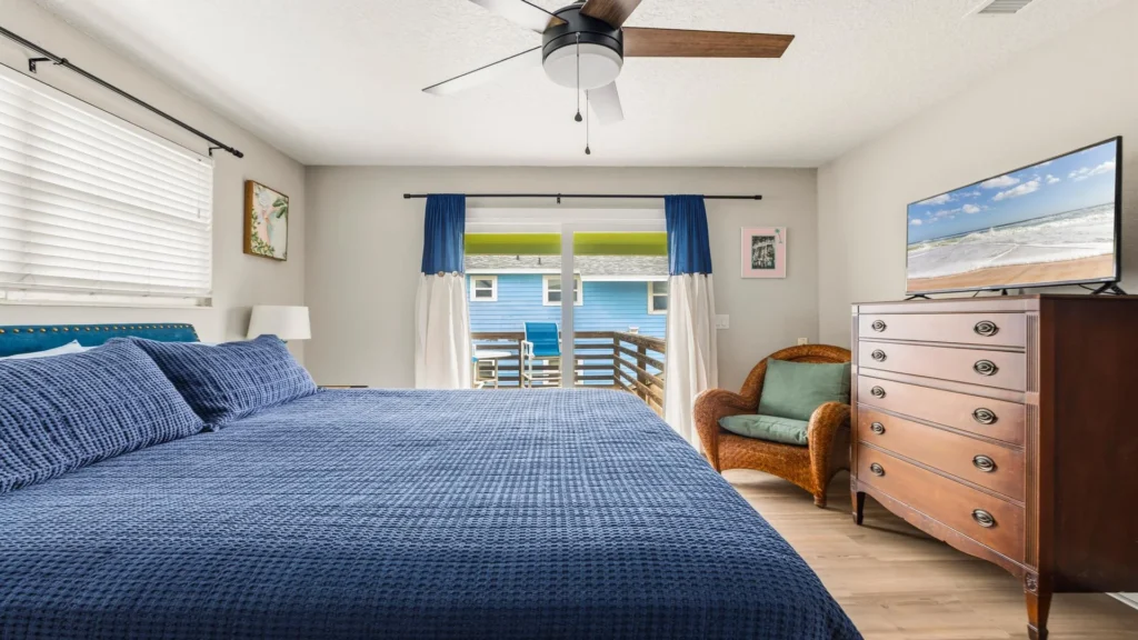 Wicker armchair with green cushion sits next to a wooden dresser topped by a flat-screen TV in the bedroom.