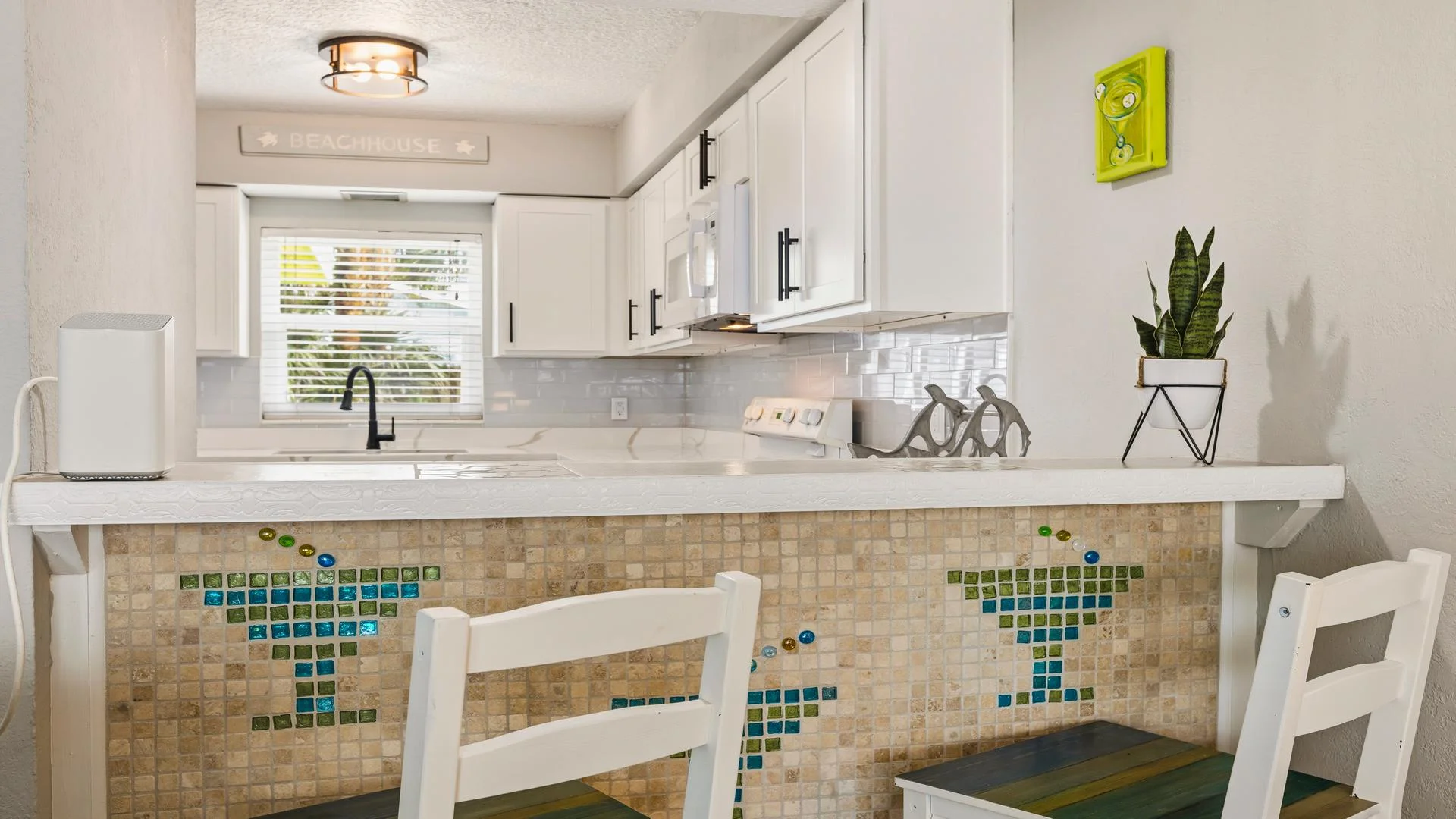 Breakfast bar with mosaic martini glass tiles, white wooden chairs, and marble-effect countertop under a ceiling light.
