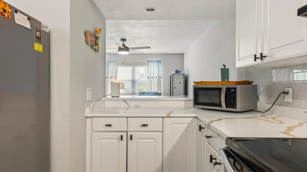 White cabinetry lines the kitchen with marble-look countertops and a stainless steel microwave on the corner.