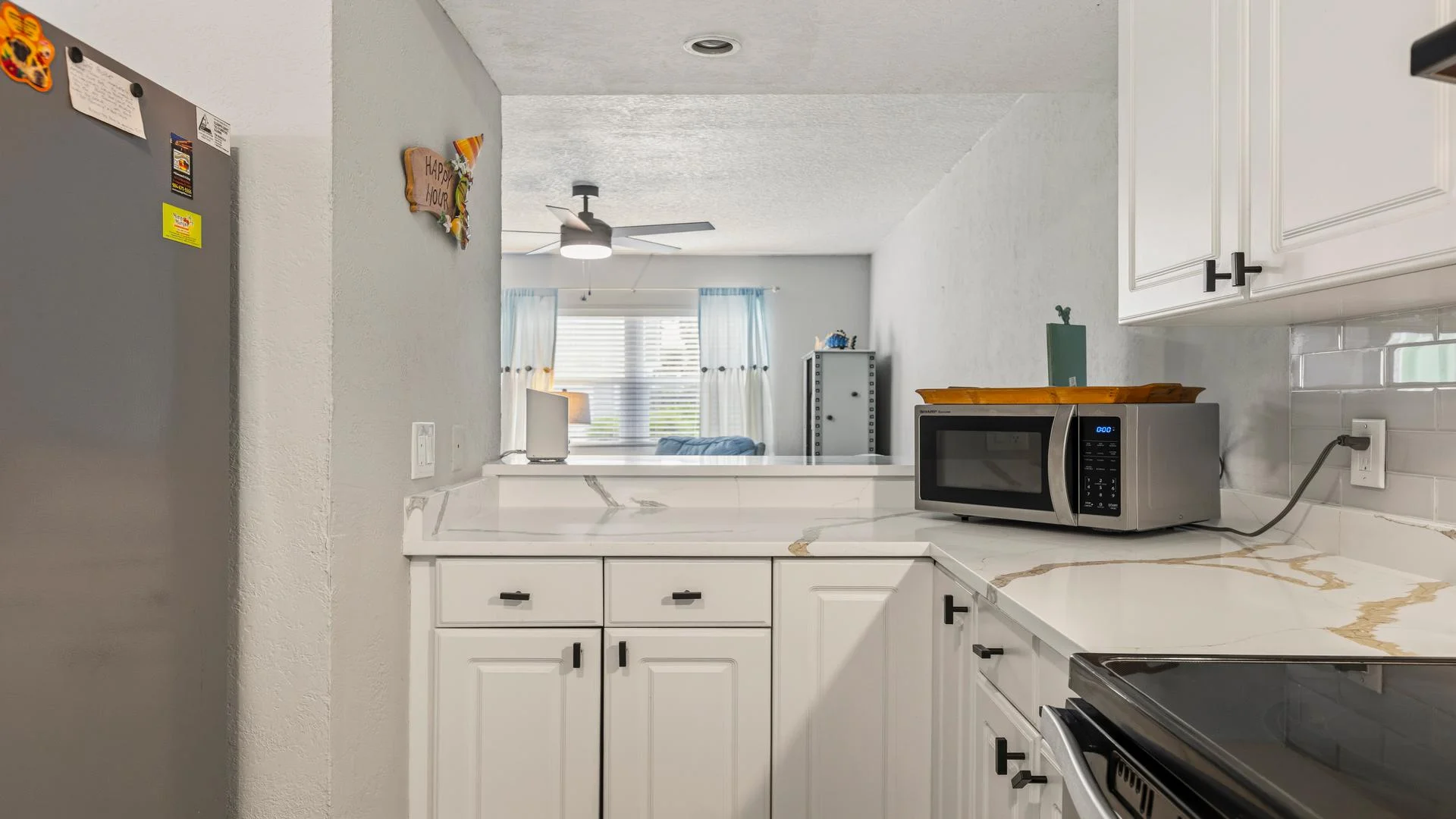 White cabinetry lines the kitchen with marble-look countertops and a stainless steel microwave on the corner.