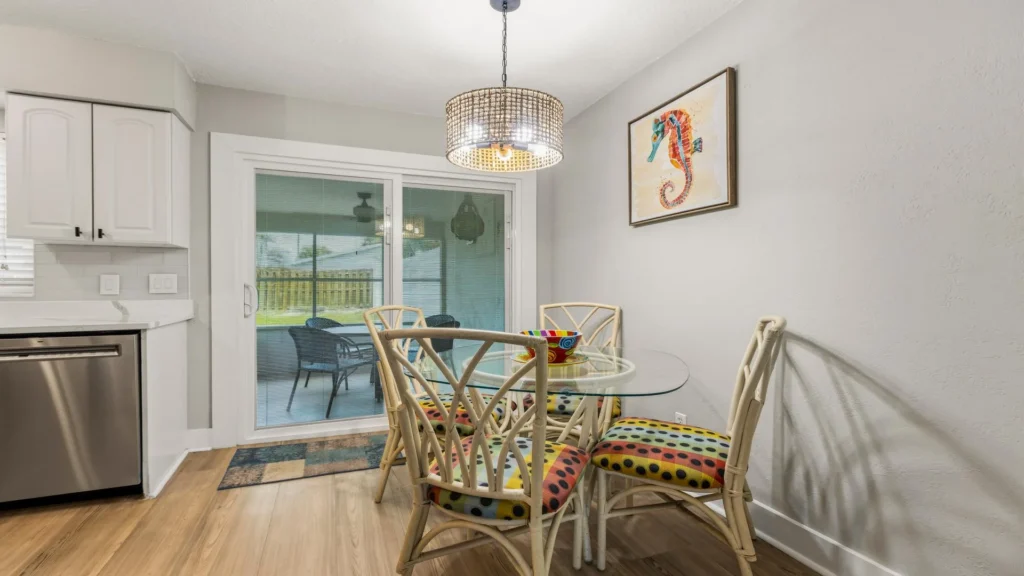 Dining area with glass-top table, rattan chairs featuring colorful polka dot cushions, and sliding doors to patio.