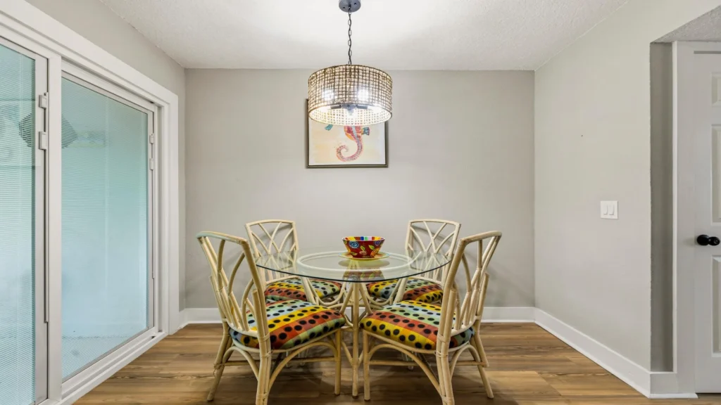 Glass-top dining table surrounded by four rattan chairs with colorful polka-dot cushions beneath a woven pendant light.