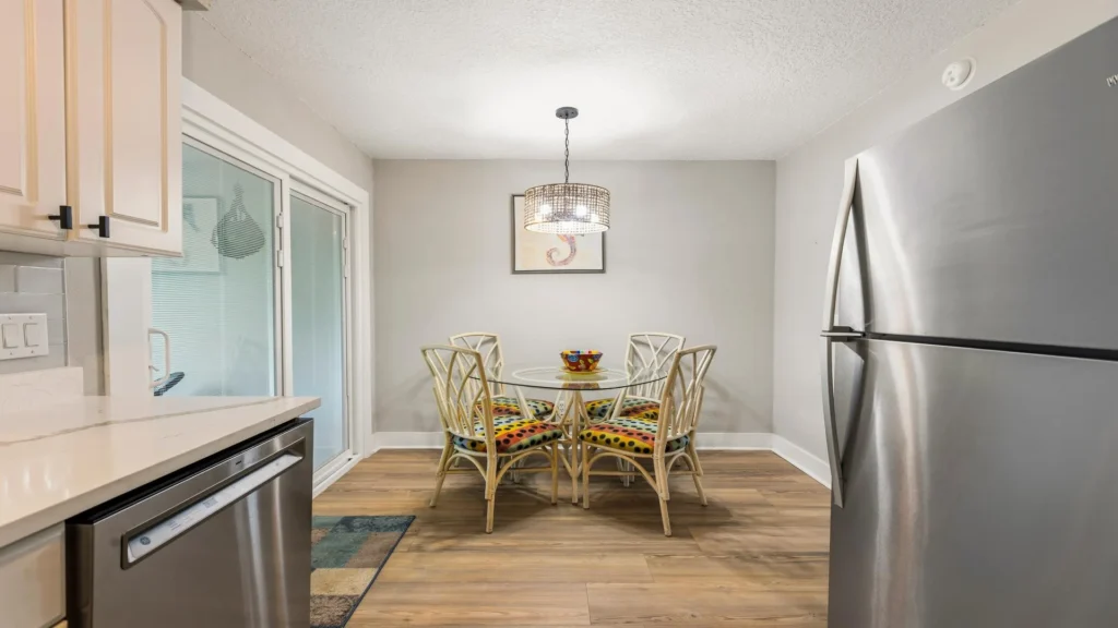 Dining area with glass-top table, colorful cushioned rattan chairs, pendant light, and wood-look flooring.