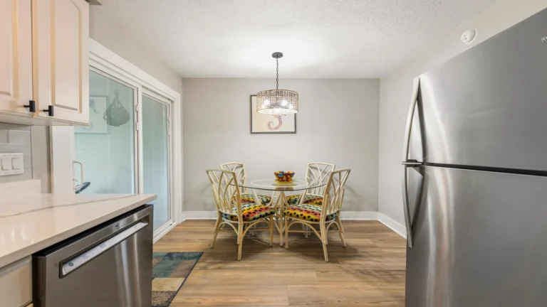 Dining area with glass-top table, colorful cushioned rattan chairs, pendant light, and wood-look flooring.