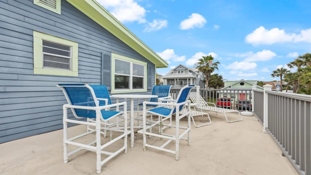 Outdoor balcony with white and blue patio seating, concrete floor, and views of neighboring homes and palm trees.