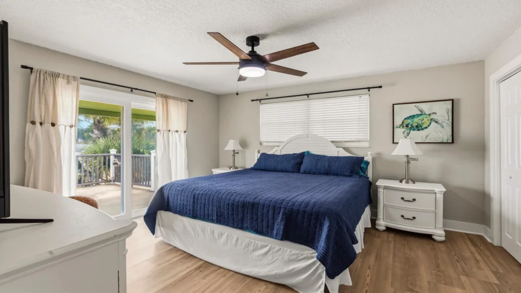 King bed with navy quilt centers the bedroom, flanked by white nightstands under a ceiling fan.
