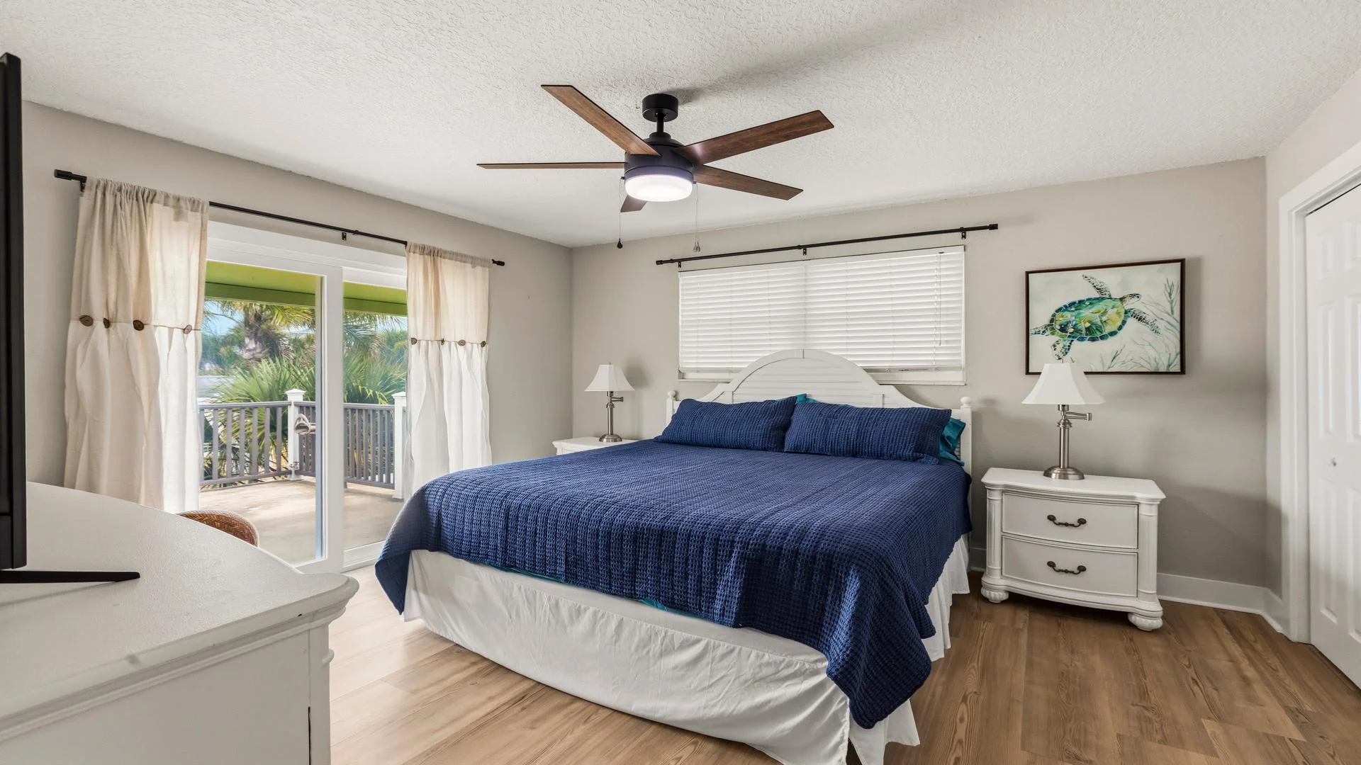 King bed with navy quilt centers the bedroom, flanked by white nightstands under a ceiling fan.