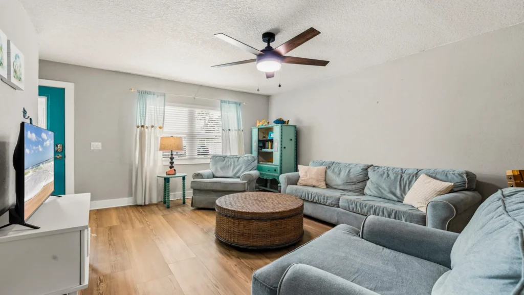 Light wood floors stretch beneath muted blue sofas and a round woven coffee table in the living room.