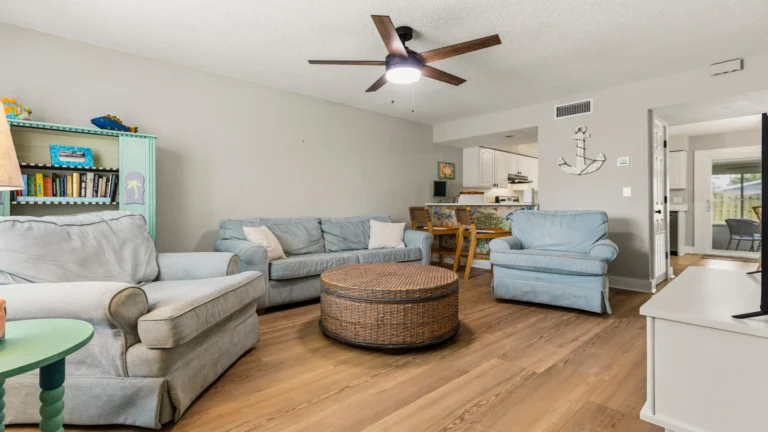 Living room with light blue upholstered seating, round wicker coffee table, and wood-look plank flooring.