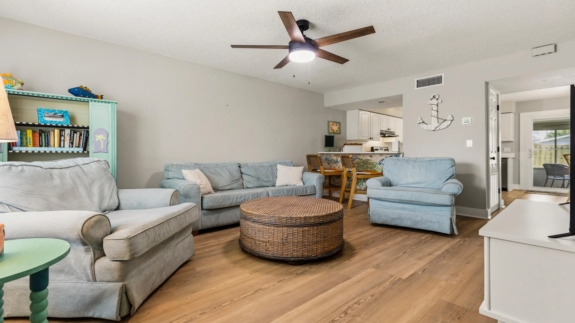 Living room with light blue upholstered seating, round wicker coffee table, and wood-look plank flooring.